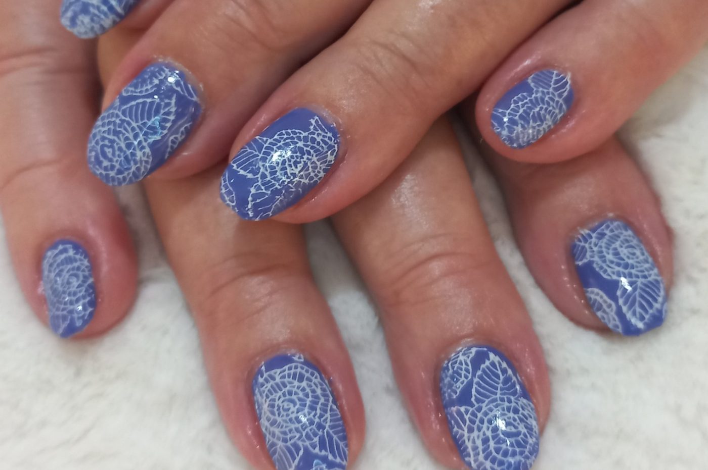 Blauwe gelnagels met witte stempelbloemen, op een wit pluche kussen