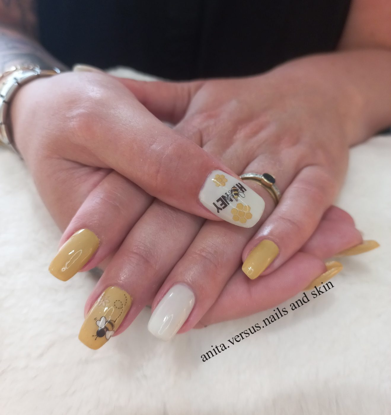 Handen met gele en witte nagels, één nagel met een bijtje, op een wit pluche kussen