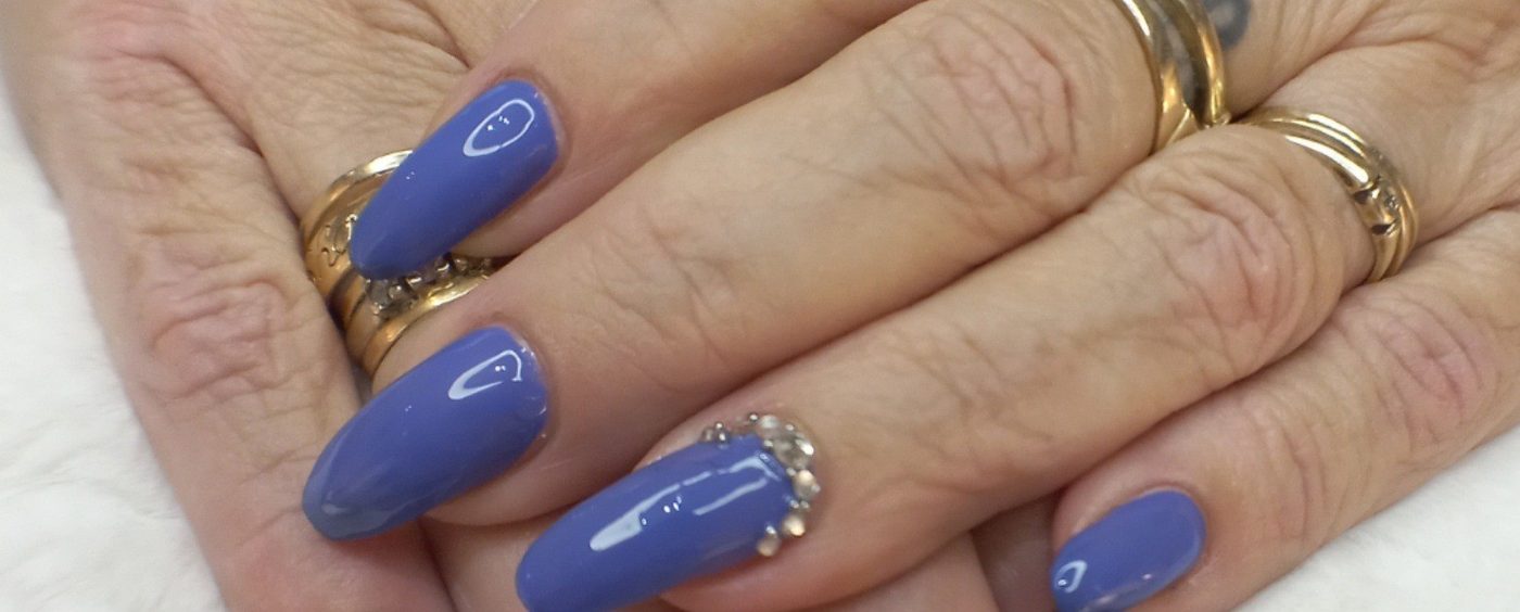 Lange blauwe nagels met steentjes, aan een hand met gouden ringen